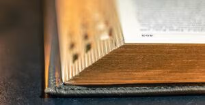 image a close-up of the corner of a book showing gold on the pages comes from a religion concept and is an open Bible on a black background